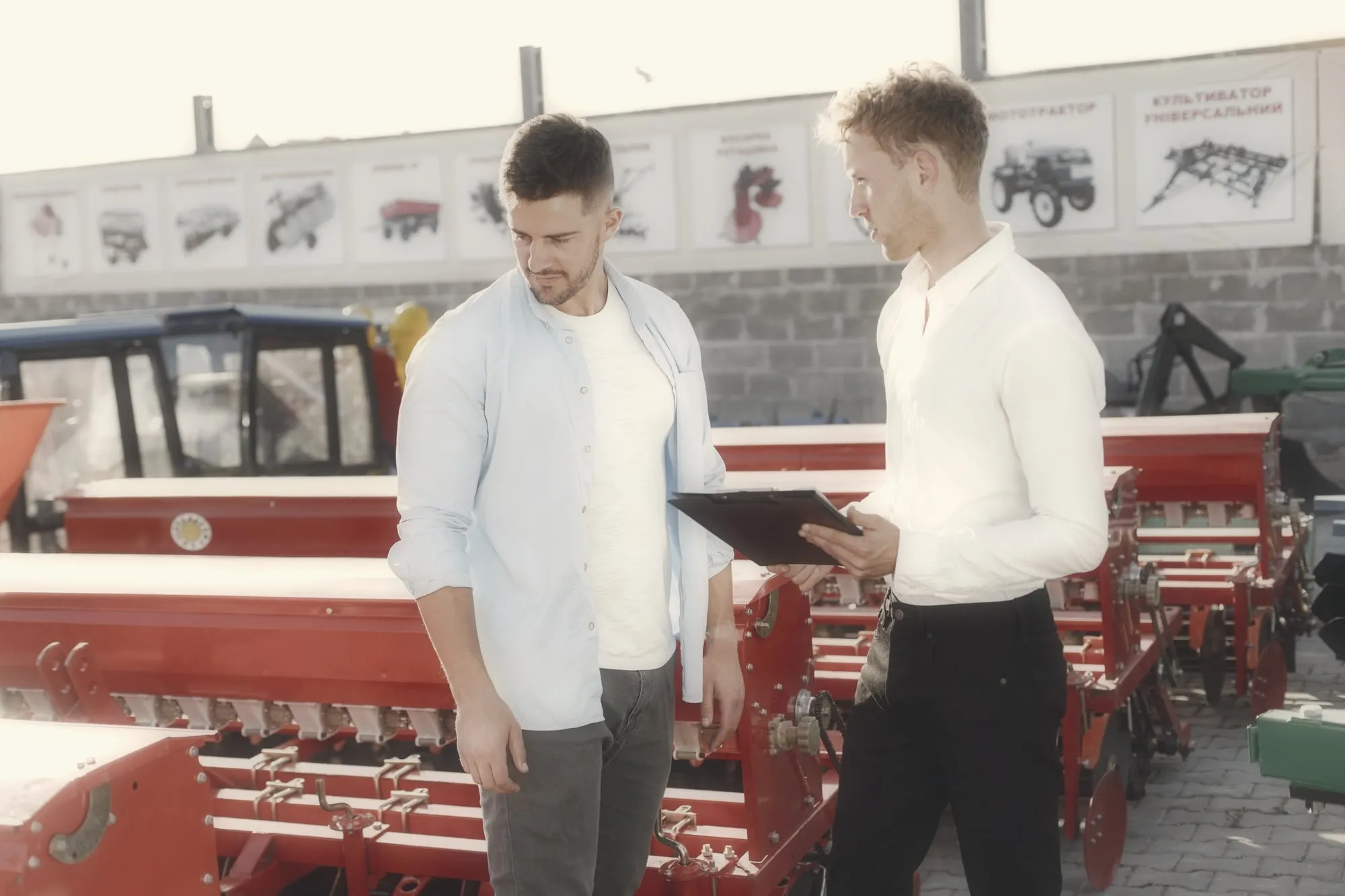 Een verkoper en een klant in gesprek naast een rij landbouwmachines op een dealerterrein