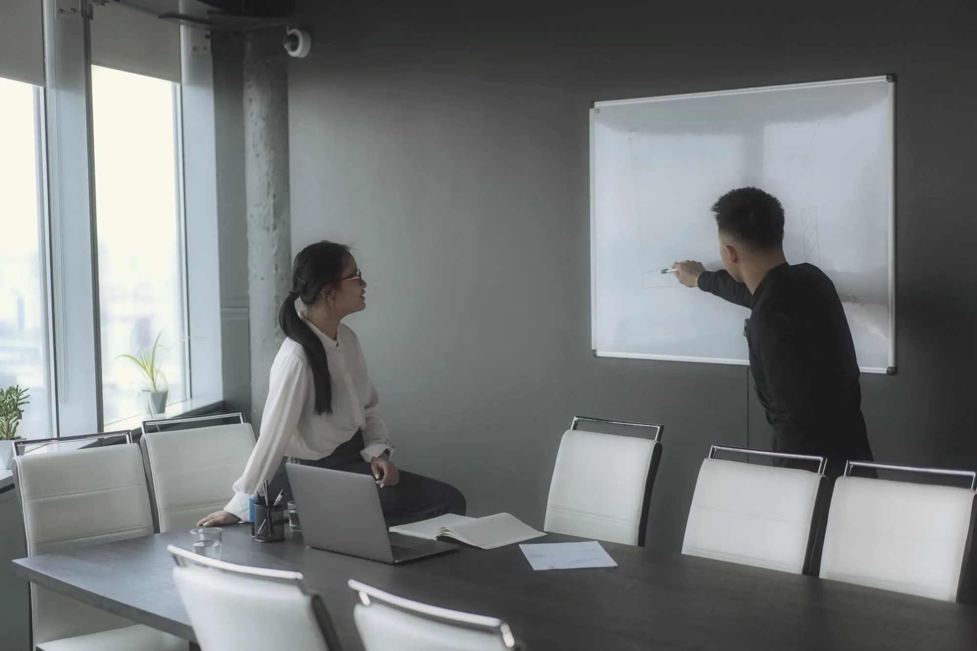 Twee collega’s werken een plan uit aan een whiteboard in een vergaderzaal